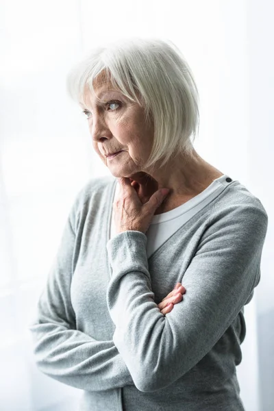 Donna anziana pensierosa in cardigan grigio guardando altrove — Foto stock