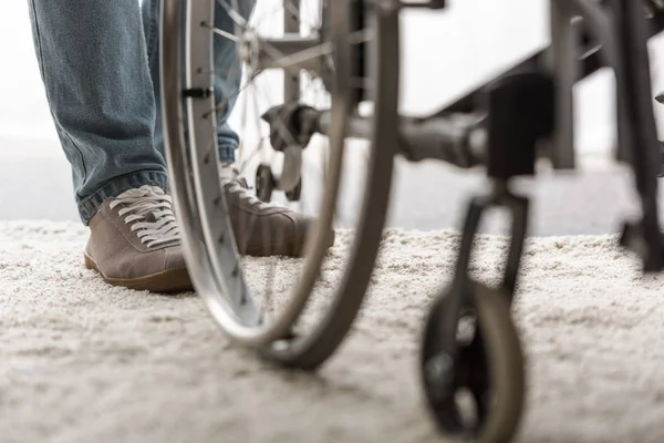 Vista recortada del hombre de pie en la alfombra cerca de la silla de ruedas - foto de stock