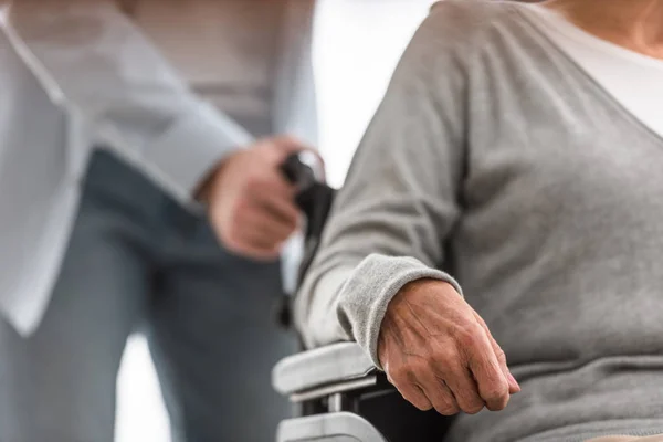 Cropped view of man carrying disabled mother on wheelchair at home — Stock Photo