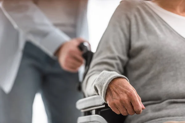 Vista recortada del hombre que lleva a la madre discapacitada en silla de ruedas en casa - foto de stock