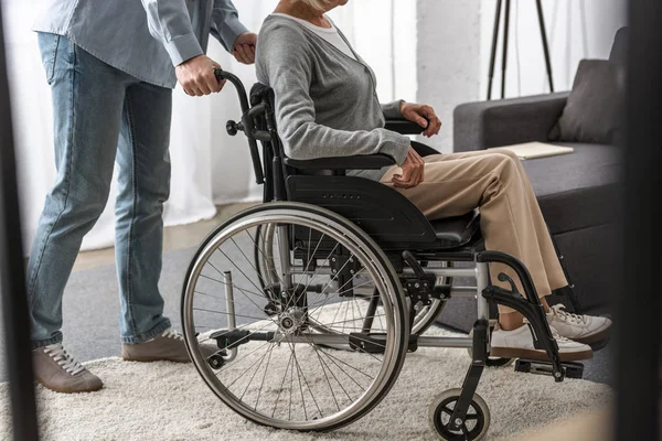 Cropped view of man carrying disabled mother on wheelchair — Stock Photo