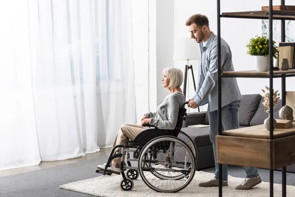 Vue de pleine longueur de l'homme portant mère handicapée en fauteuil roulant — Photo de stock