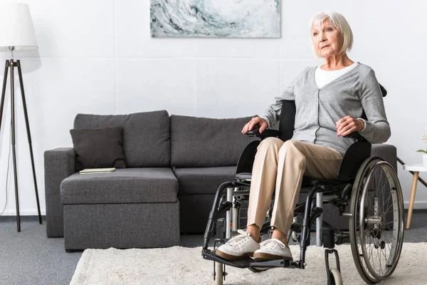 Пожилая женщина-инвалид сидит в инвалидном кресле и смотрит в сторону — стоковое фото