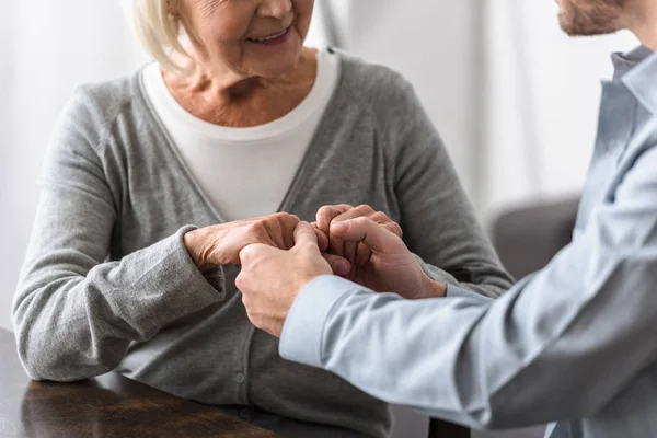 Cropped view of smiling senior woman holding hands with son — Stock Photo