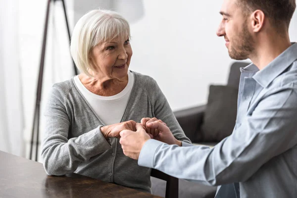 Smiling man holding hands with senior mother a home — Stock Photo