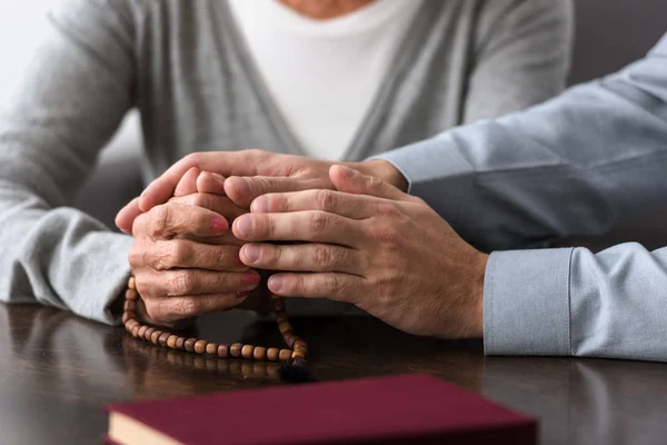 Teilansicht der Seniorin mit Rosenkranz an der Hand ihres Sohnes — Stockfoto