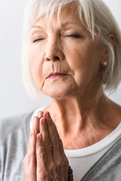 Mujer mayor mostrando por favor gesto y orando con los ojos cerrados - foto de stock