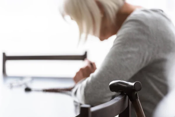 Selective focus of senior woman with grey hair and wooden walking stick on foreground — Stock Photo