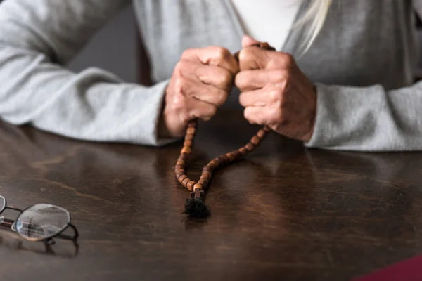 Partial view of senior woman holding wooden rosary — Stock Photo