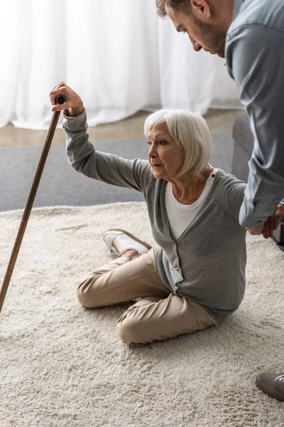 Vista recortada del hombre ayudando a la madre anciana enferma con bastón - foto de stock