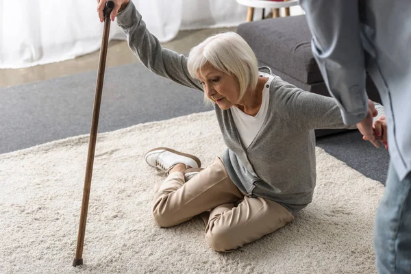 Cropped view of man helping sick senior mother with cane fallen on floor — Stock Photo