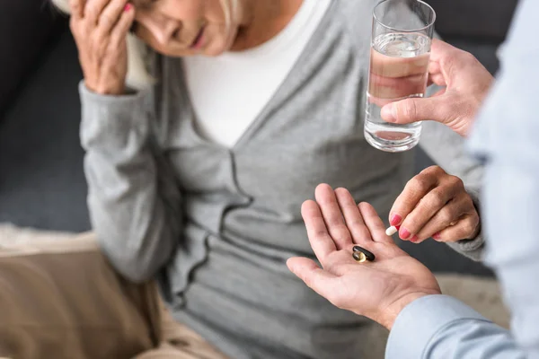 Teilansicht des Mannes, der der Seniorin ein Glas Wasser und Medizin schenkt — Stockfoto