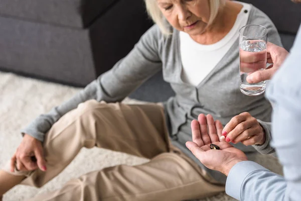 Vista parcial del hombre dando a la madre mayor vaso de agua y medicina - foto de stock