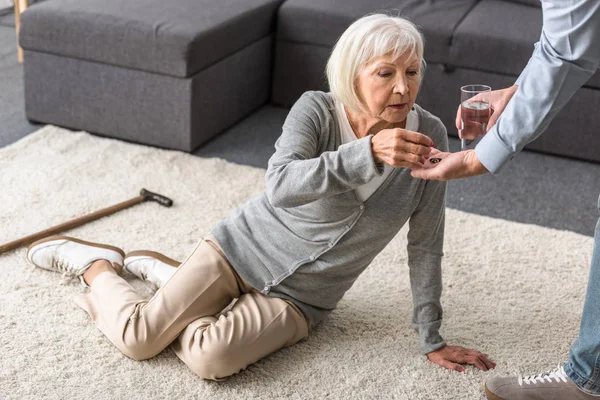 Teilansicht des Mannes, der der Seniorin ein Glas Wasser und Medizin schenkt — Stockfoto