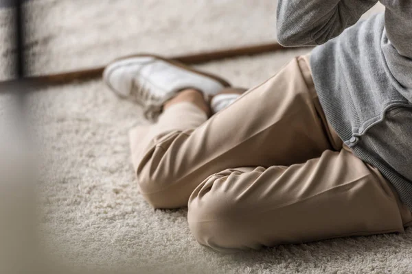 Partial view of senior woman with heart attack sitting on carpet — Stock Photo
