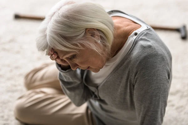 Femme âgée avec migraine assise sur le tapis et touchant le front avec la main — Photo de stock