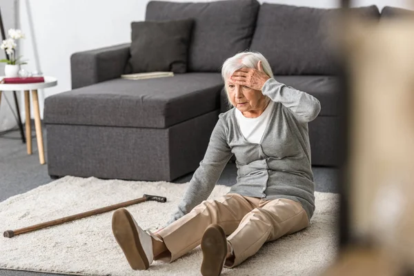 Senior woman with migraine sitting on carpet and touching forehead with hand — Stock Photo