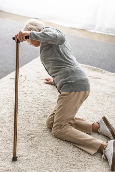 Sick senior woman with wooden cane fallen on carpet — Stock Photo