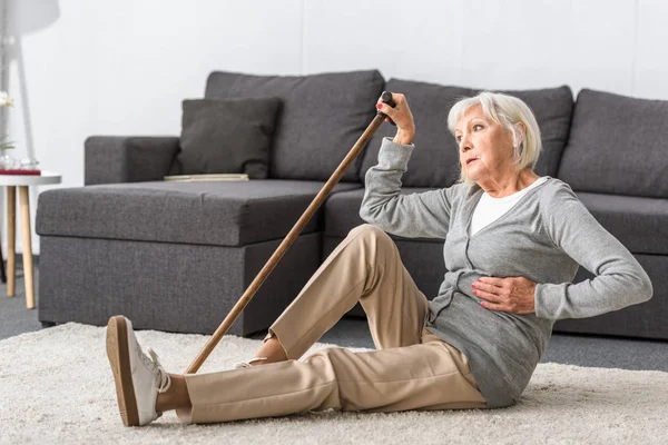 Suffering senior woman with heart attack sitting on carpet — Stock Photo