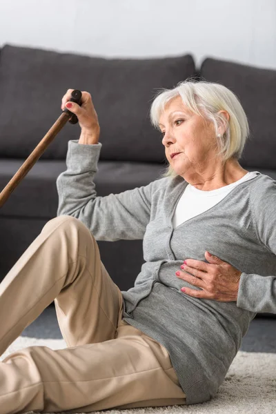 Suffering senior woman with heart attack sitting on carpet — Stock Photo