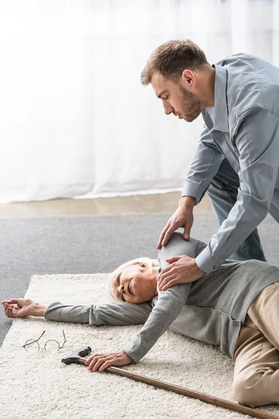 Uomo adulto con madre anziana malata sdraiata su tappeto — Foto stock