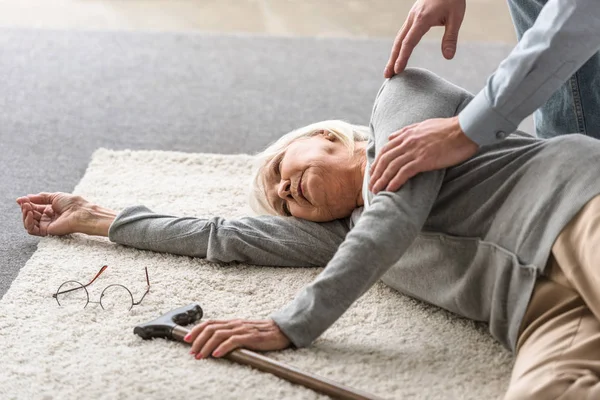 Vista ritagliata dell'uomo che aiuta la madre anziana con infarto caduto sul tappeto — Foto stock