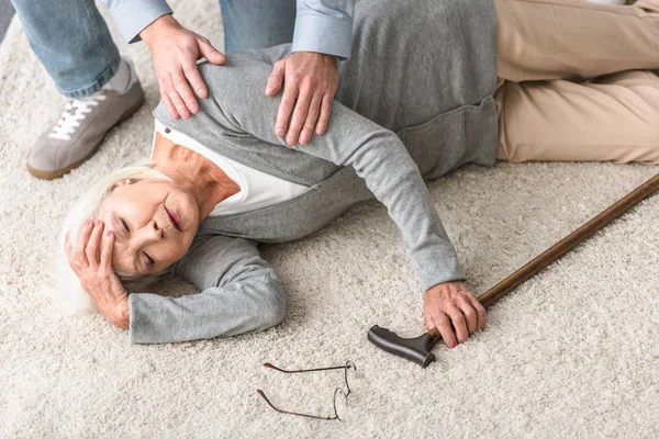 Visão cortada do homem ajudando a mãe sênior com ataque cardíaco caído no tapete — Fotografia de Stock