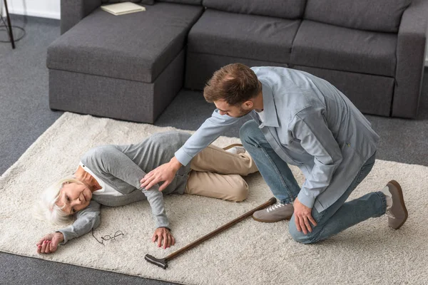 Overhead view of adult man with sick senior mother lying on carpet — Stock Photo