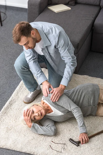 Overhead view of adult man with sick senior mother lying on carpet — Stock Photo