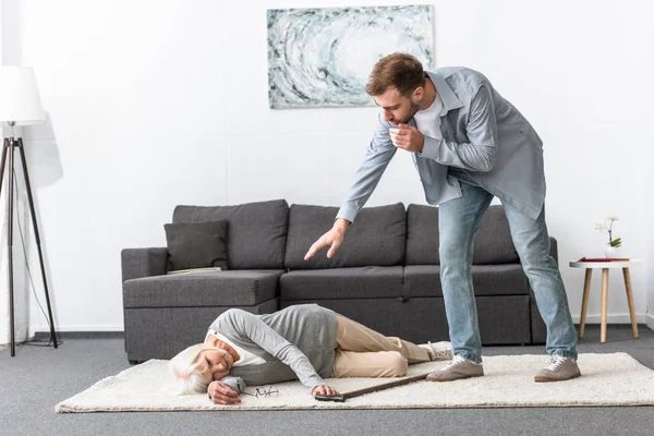 Vista completa di uomo preoccupato in piedi vicino a donna anziana sdraiata su tappeto — Foto stock