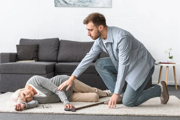 Homem preocupado perto de mulher sênior deitado no tapete — Fotografia de Stock