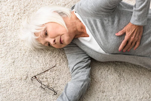Overhead view of sick senior woman lying on carpet — Stock Photo