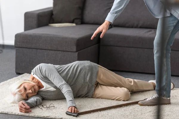Mann nähert sich Seniorin mit Gehstock auf Teppich liegend — Stockfoto