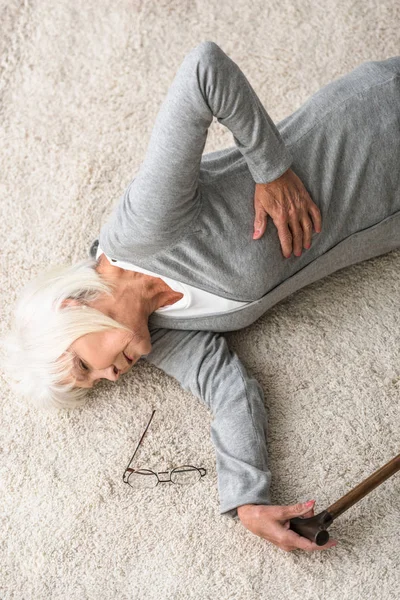 Vista aerea di malata donna anziana con bastone sdraiato su tappeto — Foto stock