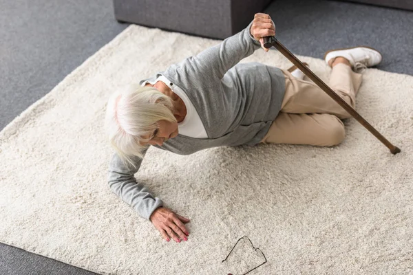 Вид зверху хвора старша жінка з палицею, що лежить на килимі — стокове фото