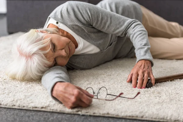 Больная пожилая женщина в очках лежит на ковре — стоковое фото
