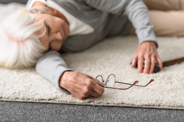 Sick senior woman with glasses lying on carpet — Stock Photo