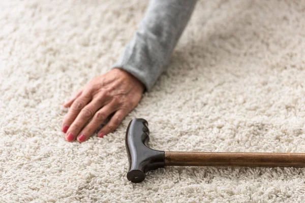 Vista ritagliata di donna anziana con canna su tappeto — Foto stock