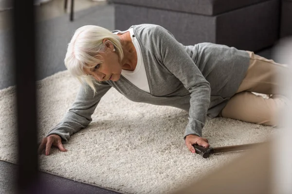 Ill senior woman with cane lying on carpet — Stock Photo