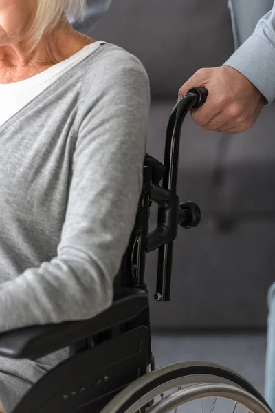 Cropped view of man carrying senior mother on wheelchair — Stock Photo