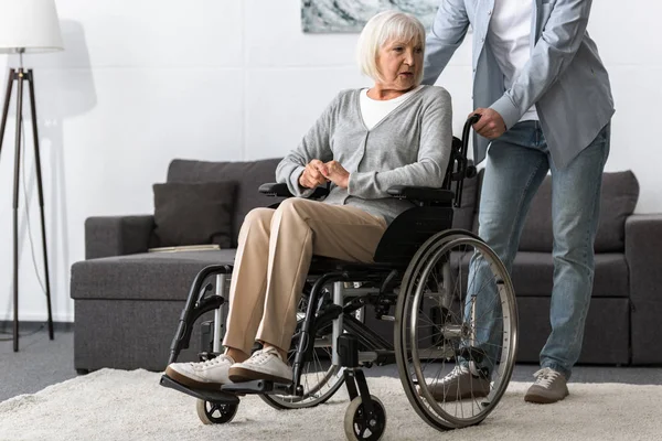 Vue recadrée de l'homme portant sa mère aînée en fauteuil roulant — Photo de stock