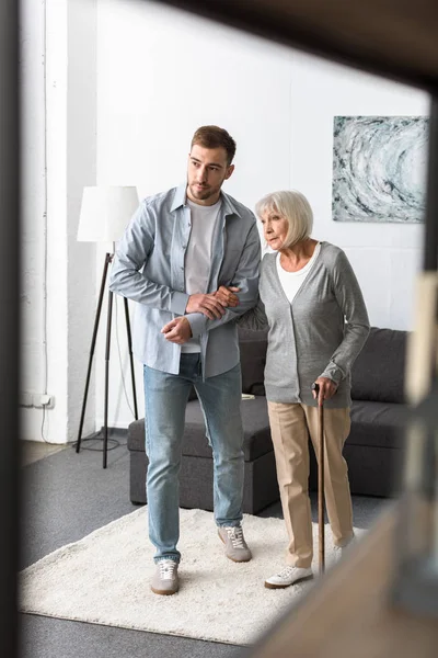 Full length view of man helping senior mother with cane at home — Stock Photo