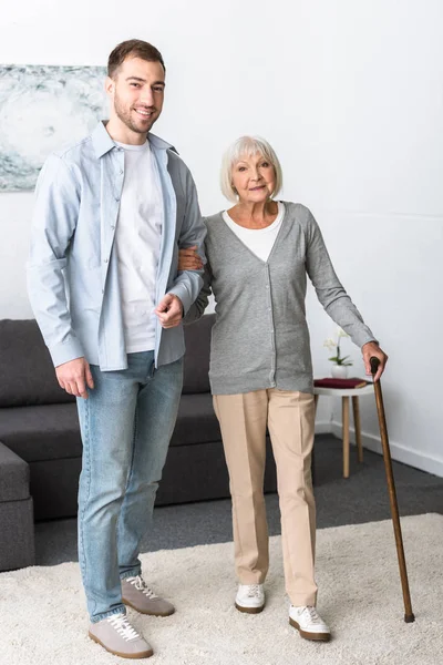 В полный рост мужчина помогает пожилой матери с тростью дома — стоковое фото
