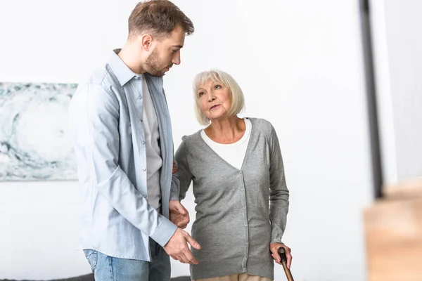 Adult son and senior mother with walking stick at home — Stock Photo