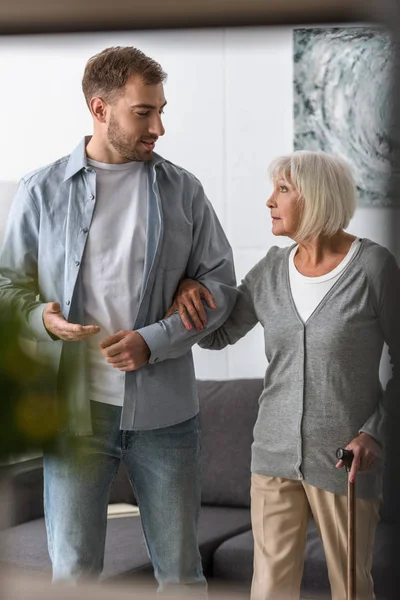 Adult son and senior mother with walking stick at home — Stock Photo