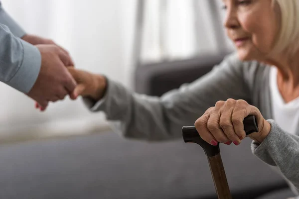 Visão cortada do homem ajudando a mãe sênior na sala de estar — Fotografia de Stock