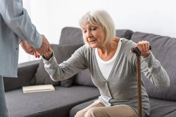 Cropped view of man helping senior mother in living room — Stock Photo