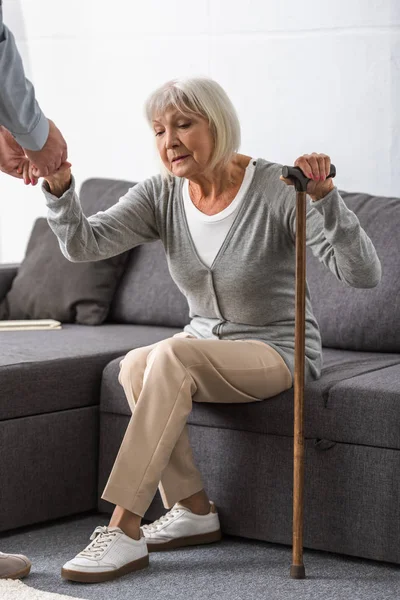 Cropped view of man helping senior mother in living room — Stock Photo