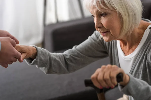 Cropped view of man helping senior mother in living room — Stock Photo