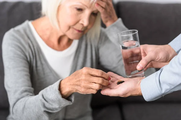 Обрезанный вид человека, дающего старшей матери стакан воды и лекарства — стоковое фото